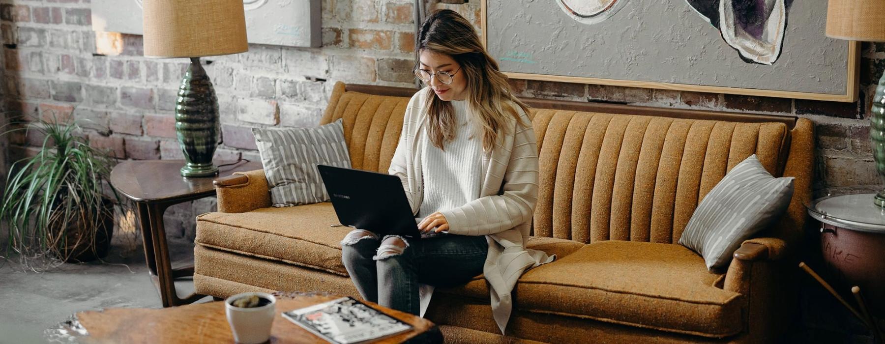 a woman sitting on a couch working on a laptop